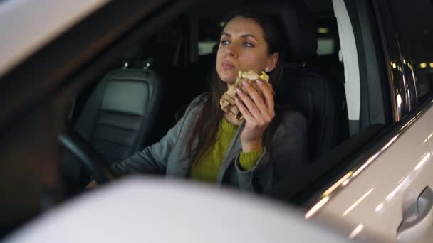 Frau isst Sandwich sitzend im Auto auf dem Parkplatz. Konzept eines modernen geschäftigen Lebens — Stockvideo