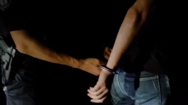 Polis memuru gece tutuklanan adama kelepçe takıyor ve onu polis arabasına götürüyor.