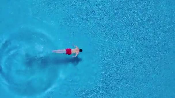 Vista desde la parte superior mientras un hombre se sumerge en la piscina y nada bajo el agua — Vídeos de Stock