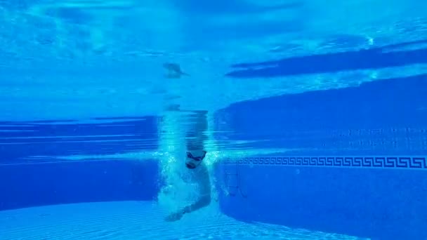 Disparos bajo el agua mientras un hombre nada bajo el agua en la piscina. Movimiento lento — Vídeos de Stock