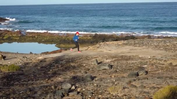 La mujer corre a lo largo de la costa pedregosa del océano. Vida activa saludable. Movimiento lento — Vídeo de stock