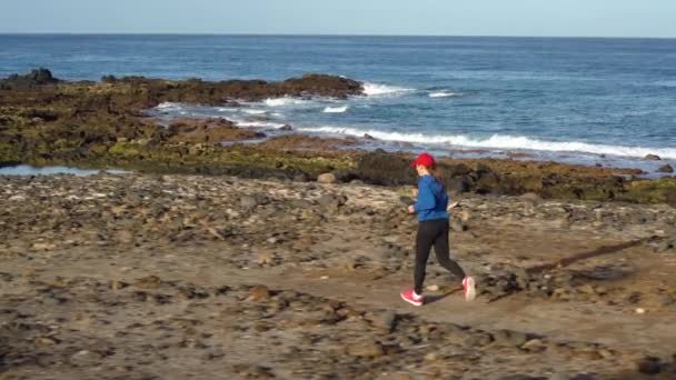 A mulher corre ao longo da costa pedregosa do oceano. Estilo de vida ativo saudável. Movimento lento — Vídeo de Stock