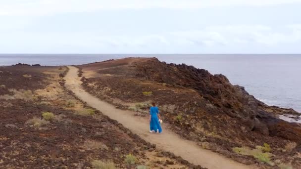 Luchtfoto van de vrouw in een mooie blauwe jurk en hoed loopt door een beschermd gebied aan de oevers van de Atlantische Oceaan. Tenerife, Canarische eilanden, Spanje — Stockvideo