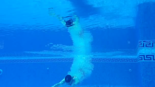 Disparos bajo el agua mientras un hombre se sumerge en la piscina y nada bajo el agua. Movimiento lento — Vídeos de Stock