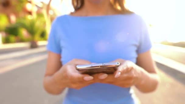 在日落时分在棕榈街上散步时使用智能手机的妇女 — 图库视频影像