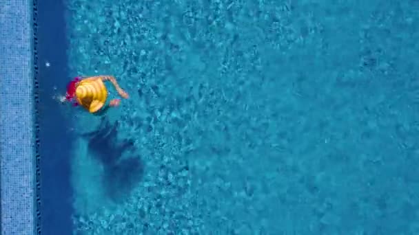 Vue du haut comme une femme en maillot de bain rouge et un grand chapeau jaune nage dans la piscine — Video