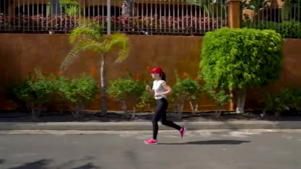 Kobieta biegnie w dół ulicy wśród drzew palmowych. Zdrowy, aktywny styl życia — Wideo stockowe
