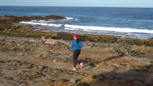 A mulher corre ao longo da costa pedregosa do oceano. Estilo de vida ativo saudável — Vídeo de Stock