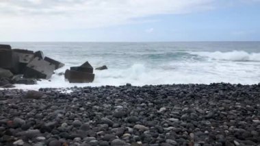 Kıyıya ulaşan büyük bir çakıl plajı ve okyanus dalgalarının timelapse. Tenerife adasının kayalık kıyısı