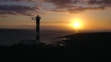 Tenerife, Kanarya Adaları, İspanya gün batımında deniz feneri silueti Faro de Rasca yükseklikten görünümü. Atlantik Okyanusu'nun vahşi sahili. Farklı hızlarda ateş: normal ve hızlı