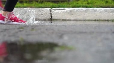 Spor ayakkabılı bir koşucunun bacakları. Spor kadını dışarıda koşuyor, çamurlu su birikintisine giriyor. Yağmurda koşan, su sıçratan tek koşucu. Yavaş çekim