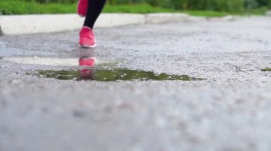 Spor ayakkabılı bir koşucunun bacakları. Spor kadını dışarıda koşuyor, çamurlu su birikintisine giriyor. Yağmurda koşan, su sıçratan tek koşucu. Yavaş çekim