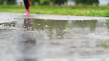 Spor ayakkabılı bir koşucunun bacakları. Spor kadını dışarıda koşuyor, çamurlu su birikintisine giriyor. Yağmurda koşan, su sıçratan tek koşucu. Yavaş çekim