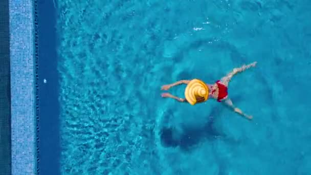 Blick von oben, als eine Frau in rotem Badeanzug und großem gelben Hut im Pool schwimmt — Stockvideo