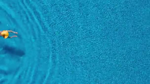 Вид сверху, как женщина в красном купальнике и большой желтой шляпе плавает в бассейне — стоковое видео