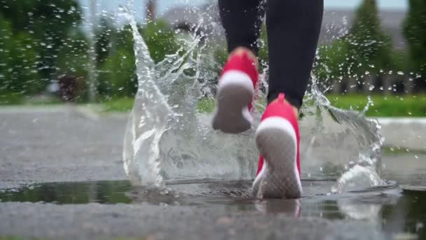 スニーカーのランナーの足。スポーツウーマンは屋外でジョギングをし、泥だらけの水たまりに足を踏み入れる。雨の中を走るシングルランナー、スプラッシュを作る — ストック動画