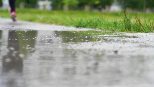 Jambes d'un coureur en baskets. Femme sportive faisant du jogging à l'extérieur, se jetant dans la flaque boueuse. Un seul coureur court sous la pluie, faisant des éclaboussures. Mouvement lent — Video