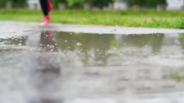 Piernas de un corredor en zapatillas. Mujer deportiva corriendo al aire libre, entrando en charco fangoso. Un solo corredor corriendo bajo la lluvia, haciendo chapoteo. Movimiento lento — Vídeo de stock