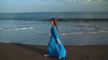 Siyah volkanik plaj boyunca yürüyen güzel mavi elbiseli kadın