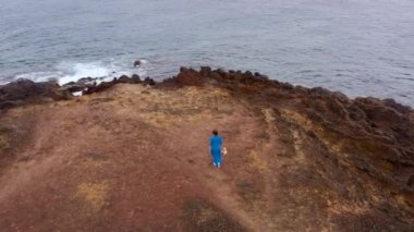 Güzel mavi elbiseli bir kadının havadan görünümü ve Atlantik Okyanusu kıyılarında bir koruma alanında bir dağın tepesine hatwalking. Tenerife, Kanarya Adaları, İspanya