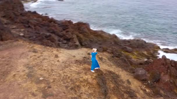 Vue aérienne de la femme dans une belle robe bleue et chapeau se dresse sur le sommet d'une montagne dans une zone de conservation sur les rives de l'océan Atlantique. Tenerife, Îles Canaries, Espagne — Video