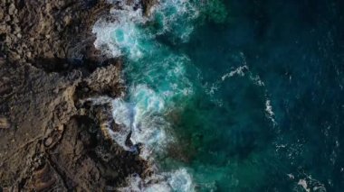 Issız bir sahil manzarası. Tenerife adasının kayalık kıyısı. Deniz dalgalarının kıyıya ulaşan hava aracı görüntüleri.