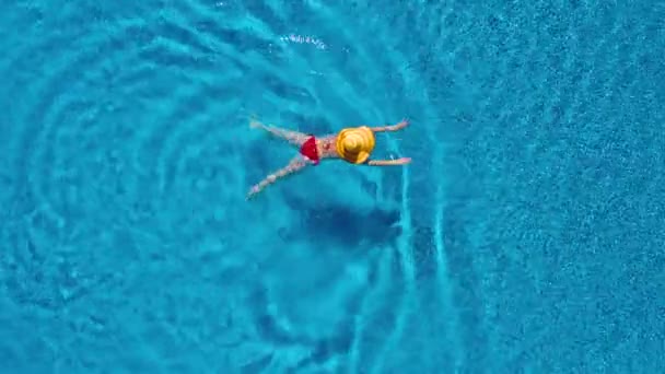 Vista de cima como uma mulher de fato de banho vermelho e um grande chapéu amarelo nada na piscina — Vídeo de Stock