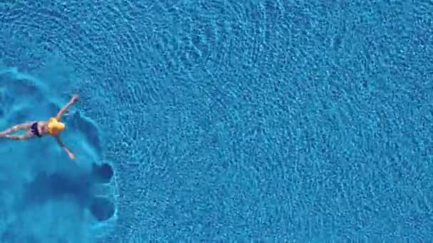 Θέα από την κορυφή ως μια γυναίκα με ένα μπλε μαγιό και ένα μεγάλο κίτρινο καπέλο κολυμπάει στην πισίνα — Αρχείο Βίντεο
