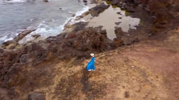 Вид с высоты женщины в красивом голубом платье и шляпе стоит на вершине горы в заповедной зоне на берегу Атлантического океана. Тенерифе, Канарские острова, Испания — стоковое видео