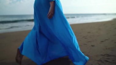 Siyah bir volkanik plaj boyunca yürüyen güzel mavi elbiseli kadın. Yavaş çekim