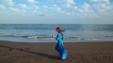 Siyah volkanik plaj boyunca uzanan güzel mavi elbiseli kadın