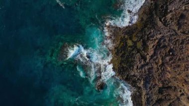 Issız bir sahil manzarası. Tenerife adasının kayalık kıyısı. Deniz dalgalarının kıyıya ulaşan hava aracı görüntüleri.
