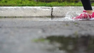 Spor ayakkabılı bir koşucunun bacakları. Spor kadını dışarıda koşuyor, çamurlu su birikintisine giriyor. Yağmurda koşan, su sıçratan tek koşucu. Yavaş çekim
