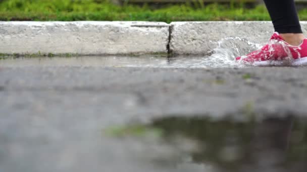 Jambes d'un coureur en baskets. Femme sportive faisant du jogging à l'extérieur, se jetant dans la flaque boueuse. Un seul coureur court sous la pluie, faisant des éclaboussures. Mouvement lent 