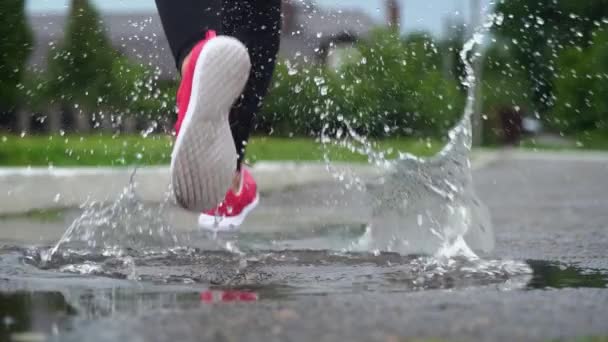 Nohy běžce v teniskách. Sportovní žena běhají venku a šlápne na blátivou louži. Jeden běžec běží v dešti a dělá šplouchnutí. Pohled zpět. Zpomaleně — Stock video