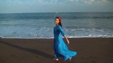 Siyah volkanik plaj boyunca yürüyen güneş gözlüğü ve mavi elbiseli kadın