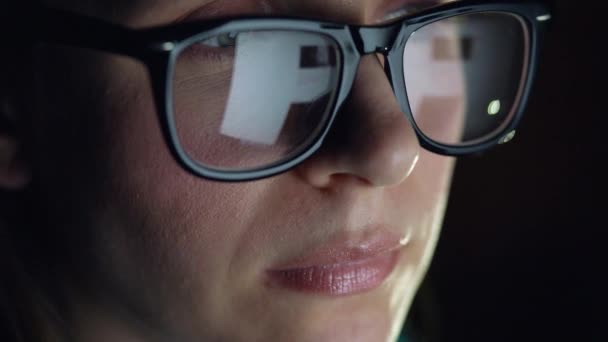 Mulher de óculos olhando no monitor e navegando na Internet. A tela do monitor é refletida nos óculos — Vídeo de Stock