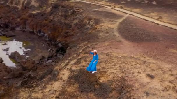 Vista aérea de la mujer en un hermoso vestido azul y sombrero se encuentra en la cima de una montaña en un área de conservación a orillas del Océano Atlántico. Tenerife, Islas Canarias, España — Vídeo de stock