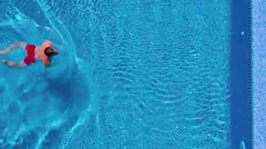Kırmızı şortla adamın havadan görünümü havuzda yüzer ve dışarı çıkar.