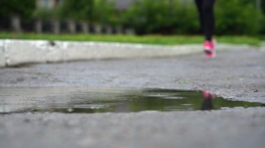 Spor ayakkabılı bir koşucunun bacakları. Spor kadını dışarıda koşuyor, çamurlu su birikintisine giriyor. Yağmurda koşan, su sıçratan tek koşucu. Yavaş çekim