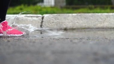 Spor ayakkabılı bir koşucunun bacakları. Spor kadını dışarıda koşuyor, çamurlu su birikintisine giriyor. Yağmurda koşan, su sıçratan tek koşucu. Yavaş çekim