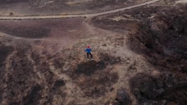 Koşu sonrası spor giyimli kadının havadan görünümü bir kayanın üzerinde duruyor ve Atlantik Okyanusu kıyılarındaki bir koruma alanında manzaranın keyfini çıkarıyor. Tenerife, Kanarya Adaları, İspanya