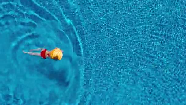 Vue du haut comme une femme en maillot de bain rouge et un grand chapeau jaune nage dans la piscine — Video