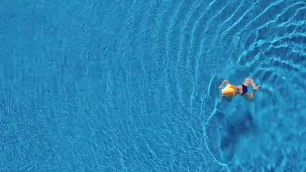 Vista desde la parte superior como una mujer en traje de baño azul y un gran sombrero amarillo nada en la piscina — Vídeos de Stock