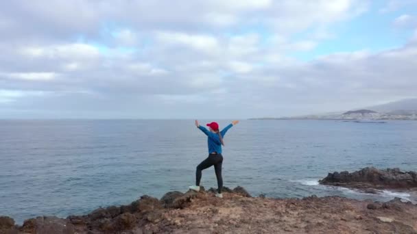 Luchtfoto van de vrouw in de sportkleding na het joggen staat op de top van een rots en geniet van het landschap in een beschermd gebied aan de oevers van de Atlantische Oceaan. Tenerife, Canarische eilanden, Spanje — Stockvideo