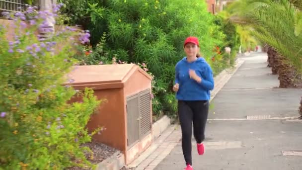 Жінка біжить по вулиці серед тропічної алеї — стокове відео