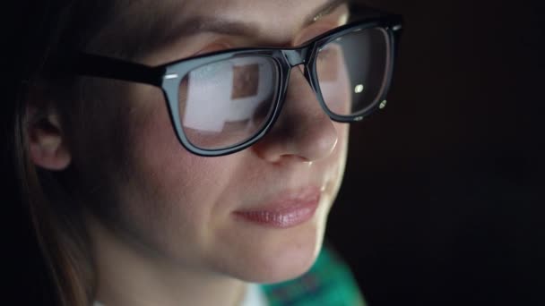 Mujer con gafas mirando en el monitor y navegando por Internet. La pantalla del monitor se refleja en las gafas — Vídeo de stock