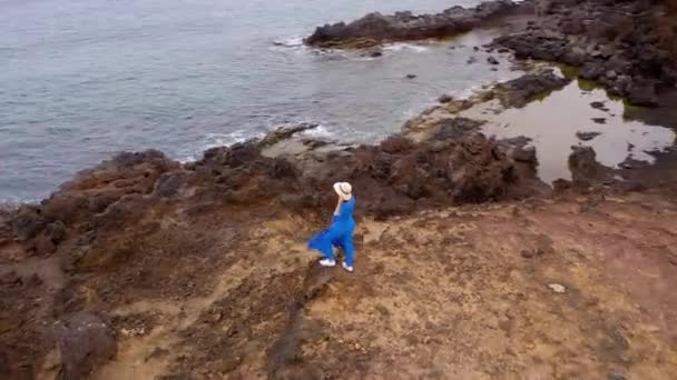 Aerial syn på kvinnan i en vacker blå klänning och hatt står på toppen av ett berg i ett naturskyddsområde vid stranden av Atlanten. Teneriffa, Kanarieöarna, Spanien — Stockvideo