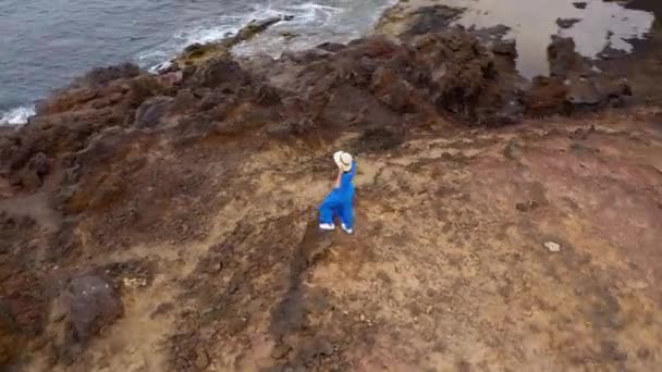 Luchtfoto van de vrouw in een mooie blauwe jurk en hoed staat op de top van een berg in een beschermd gebied aan de oevers van de Atlantische Oceaan. Tenerife, Canarische eilanden, Spanje — Stockvideo