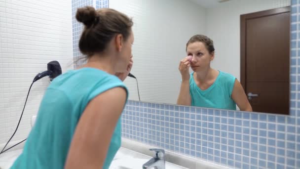 Mooie vrouw toepassing basis onder make-up of stichting met spons voor badkamerspiegel — Stockvideo